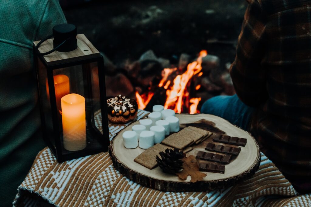a person sitting in front of a campfire with a tray of marshmallow