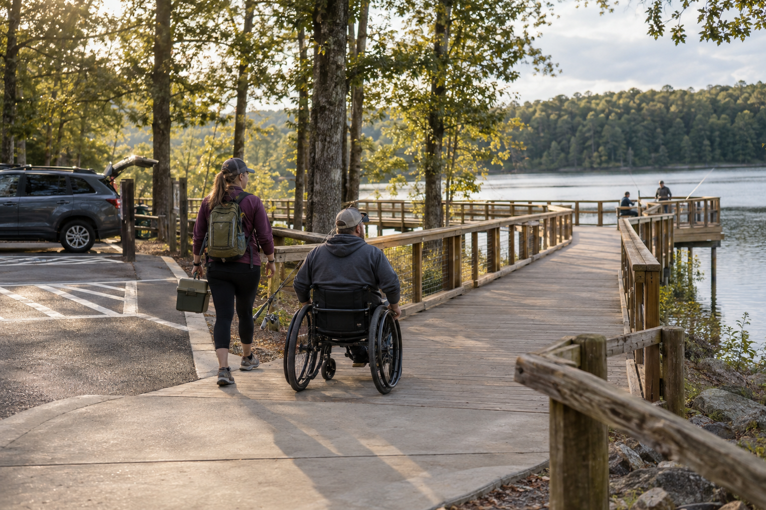 Camper using a wheelchair and a companion following a step-free boardwalk from accessible parking to a lakeside fishing platform.